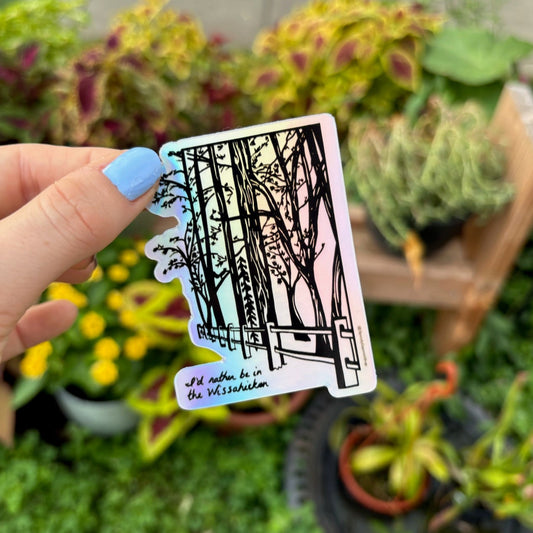 Hand holding a Wissahickon Valley Park sticker with the Forbidden Drive trail with a blurred garden background