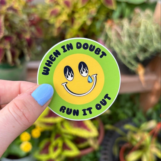 Hand holding a sticker with a smiley face and text in front of potted plants. Text says "when in double run it out."