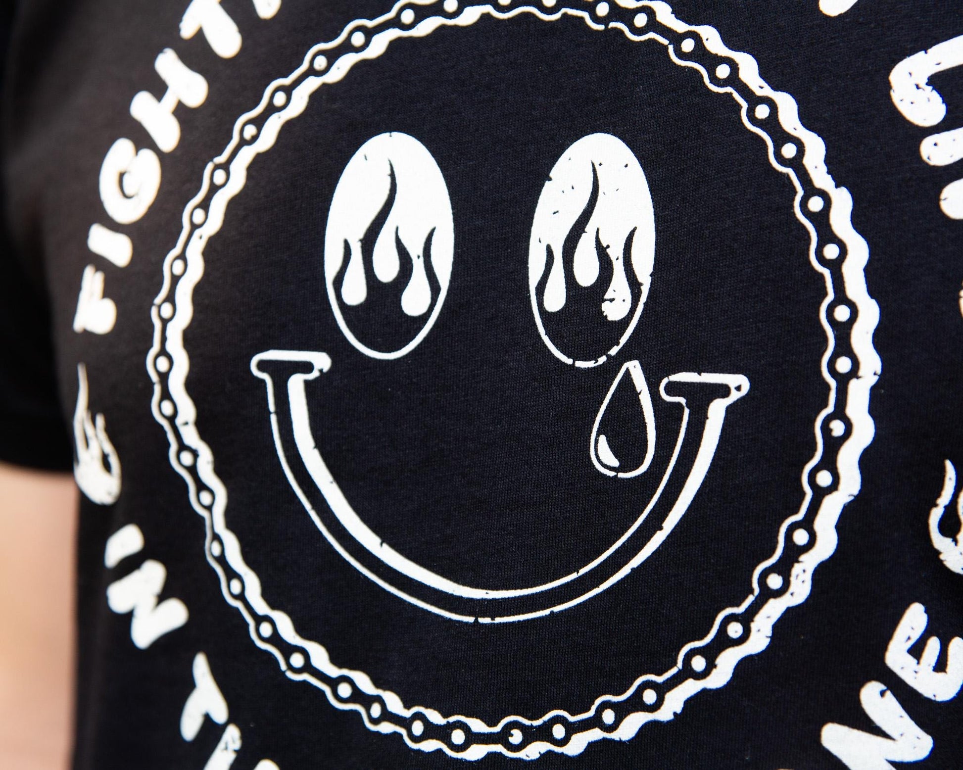 Black Tshirt with a White Illustration of a happy face with Flames in the Eyes that says "Fighting for my life in the bike lane " around the illustration 